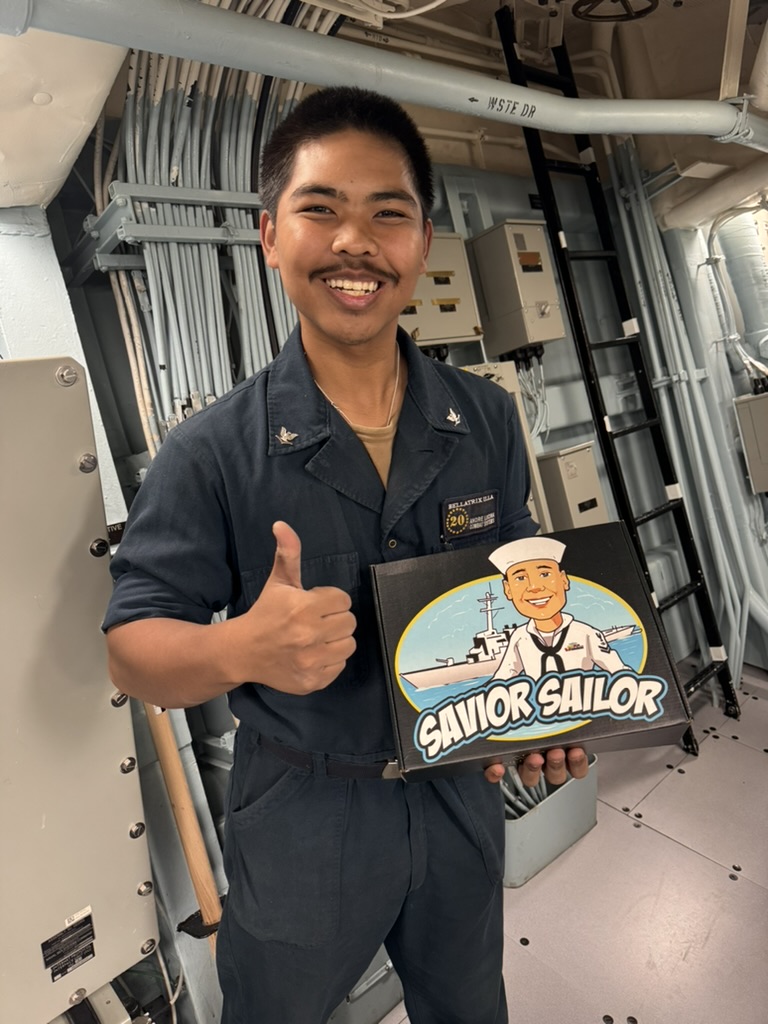 Sailor giving a thumbs up while holding his Savior Sailor care package below decks