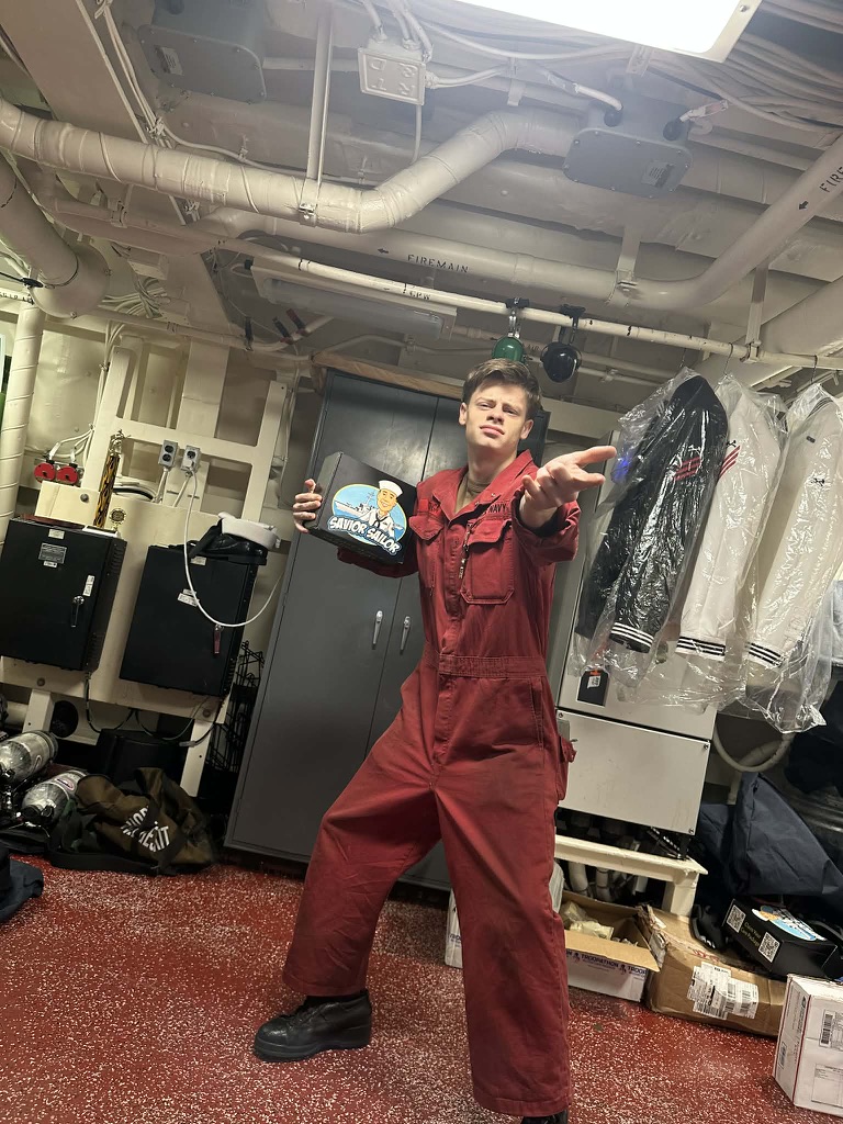 Sailor in red coveralls striking a fun pose with his Savior Sailor care package