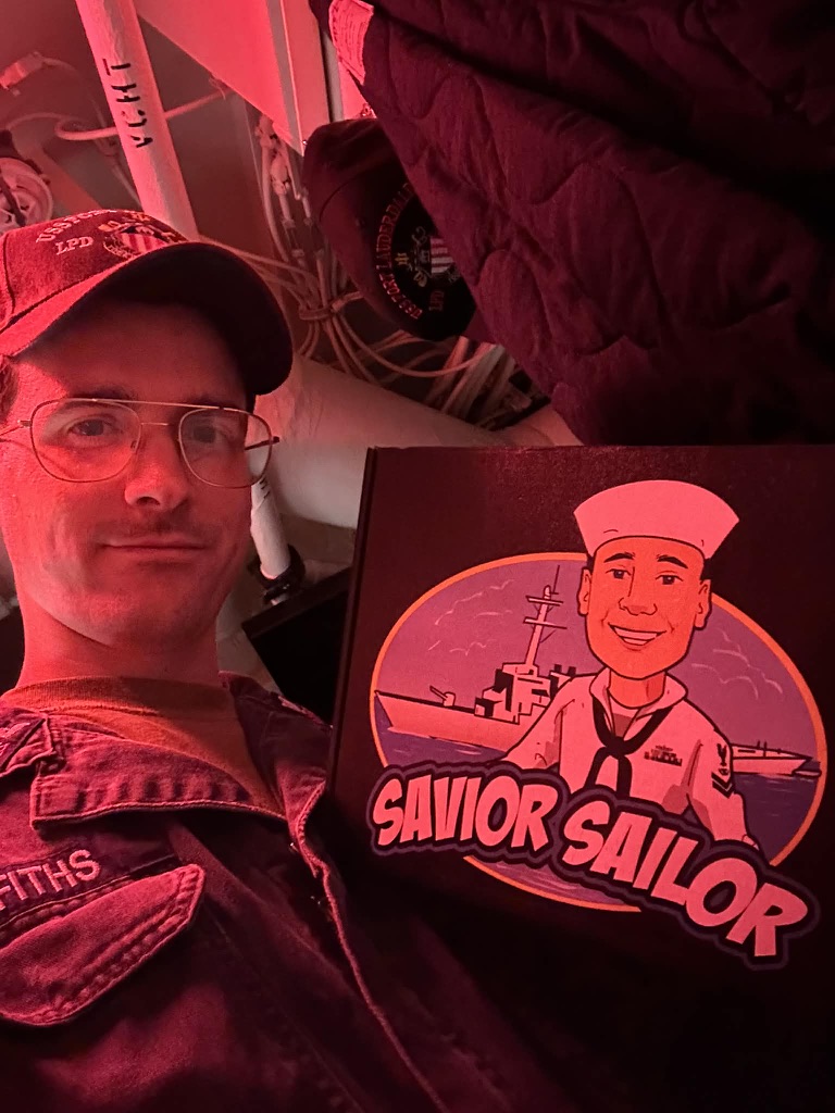 Sailor taking a selfie with his Savior Sailor care package in the red-lit berthing area